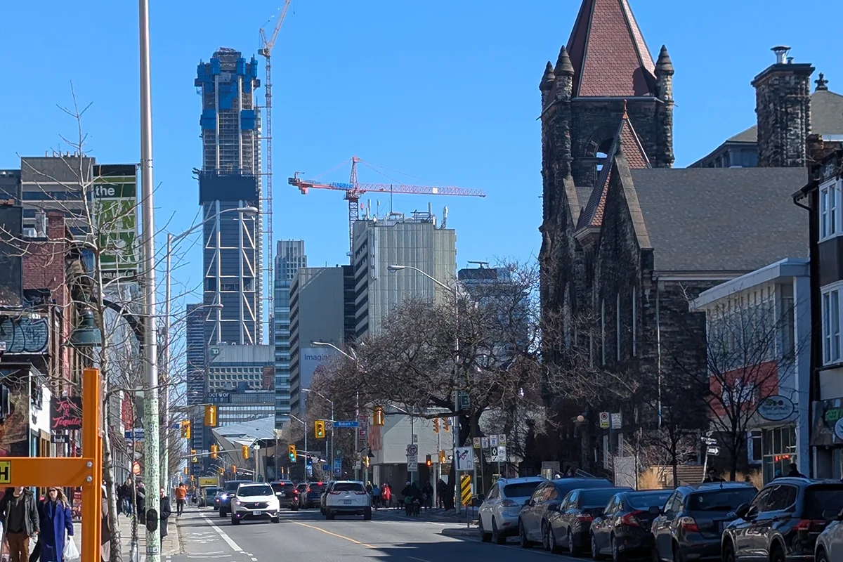 Tall skyscraper under construction with crane in distance with busy street in foreground
