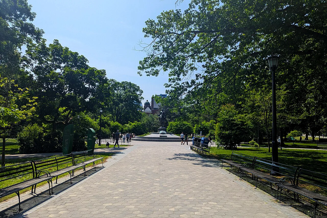 walkway through park with trees and benches on sunny summer day